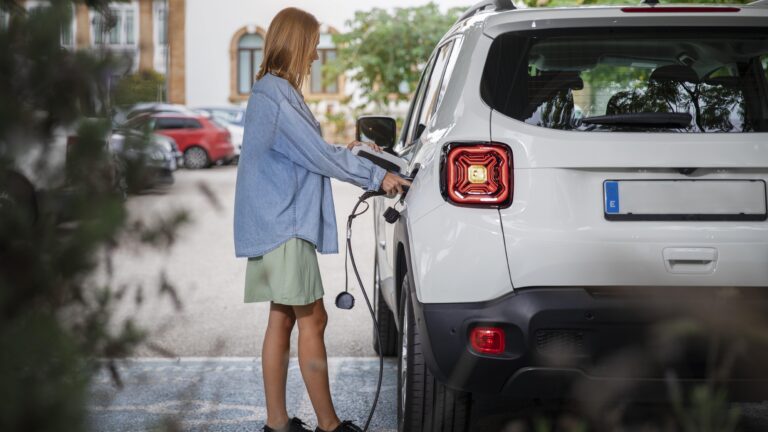 Femme qui recharge son véhicule électrique avec des plantes au premier plan