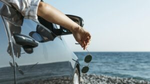 Voiture orienté vers la mer avec une main qui sort du véhicule en été